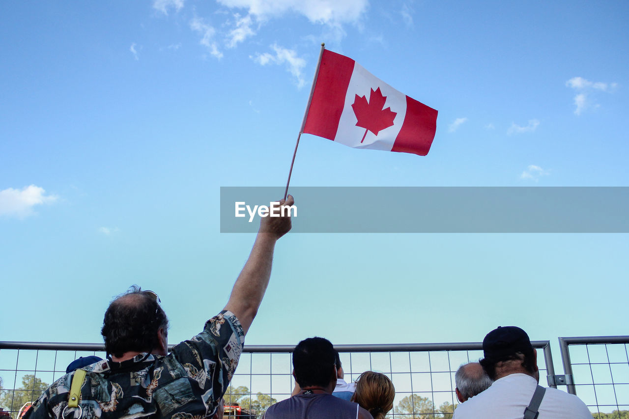 Rear view of man waving canadian flag in stadium against sky