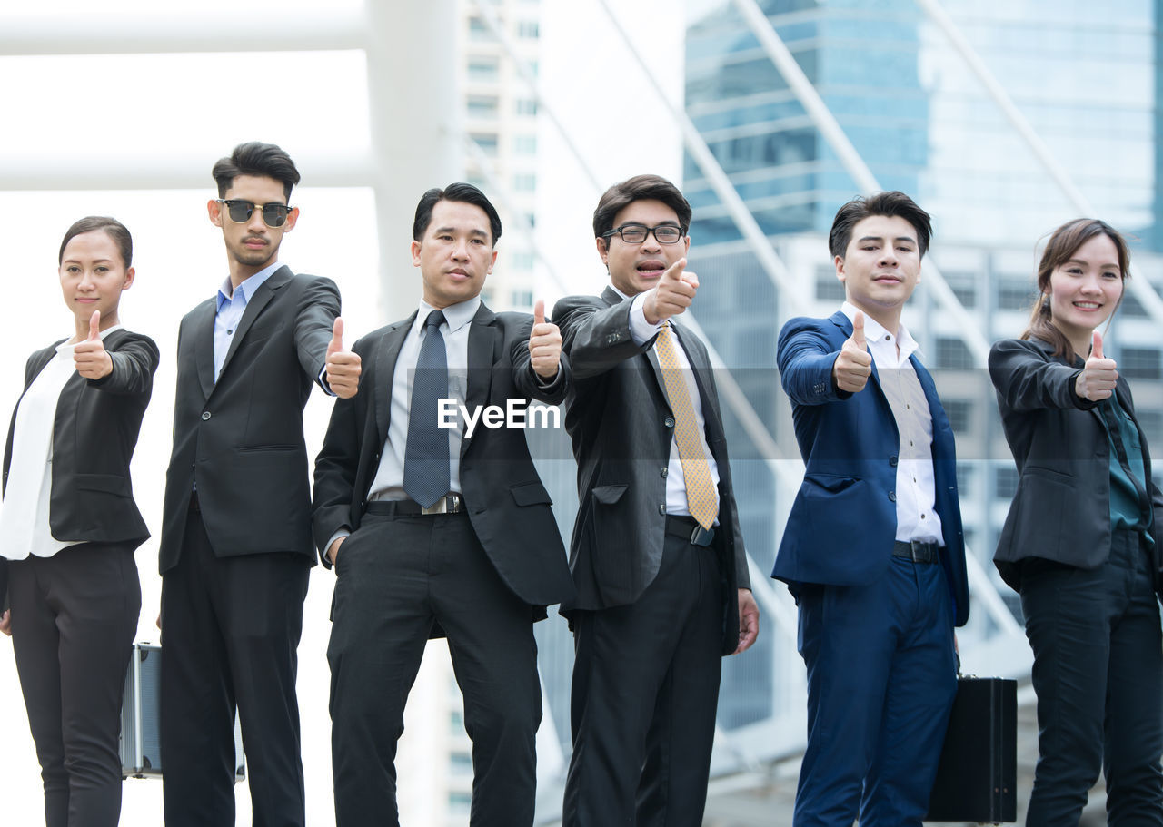 Portrait of businesspeople showing thumbs up against buildings in city