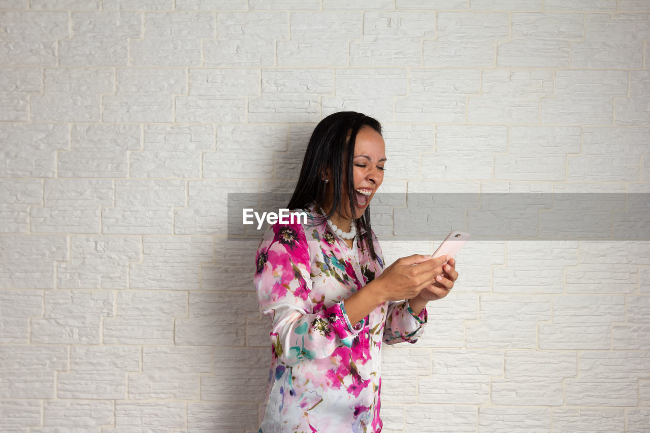 WOMAN HOLDING SMART PHONE WHILE STANDING ON WALL