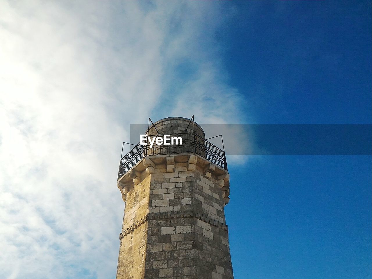 Low angle view of tower against cloudy blue sky on sunny day
