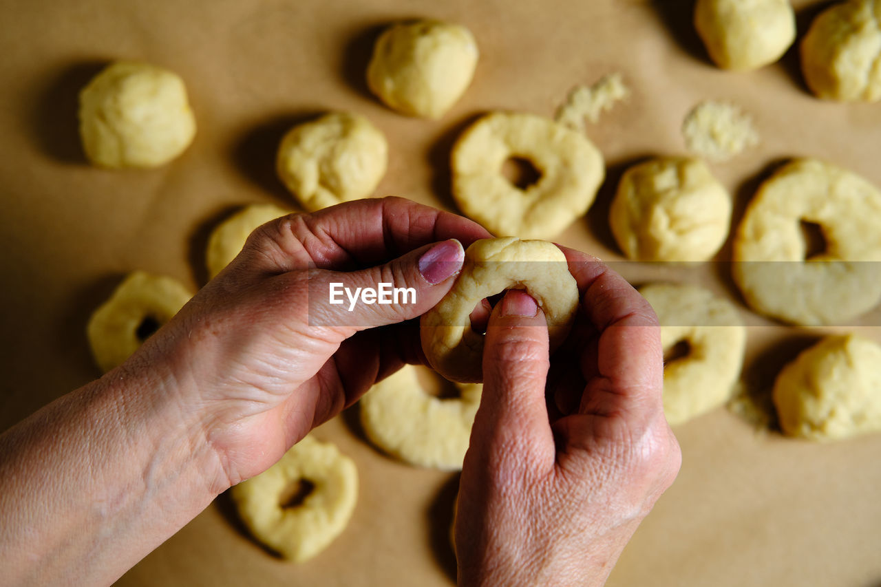 Top view of anonymous woman making rings from soft dough while preparing doughnuts over table in kitchen