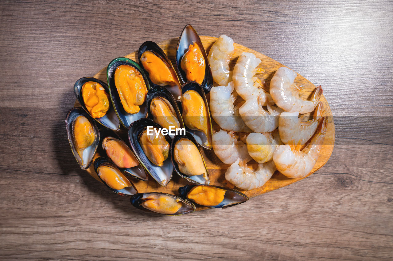 Flat kitchen table raw mussels and shrimp lie on a wooden plate. sea food. mediterranean diet