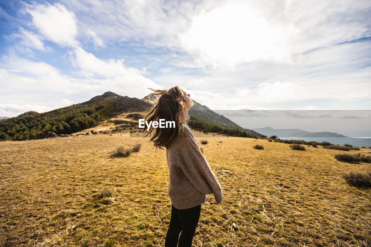 Side view of young gentle female traveler in casual outfit with eyes closed against mount in sunlight in spain