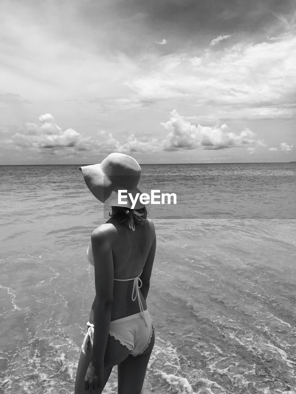 Woman wearing bikini while standing at beach against sky