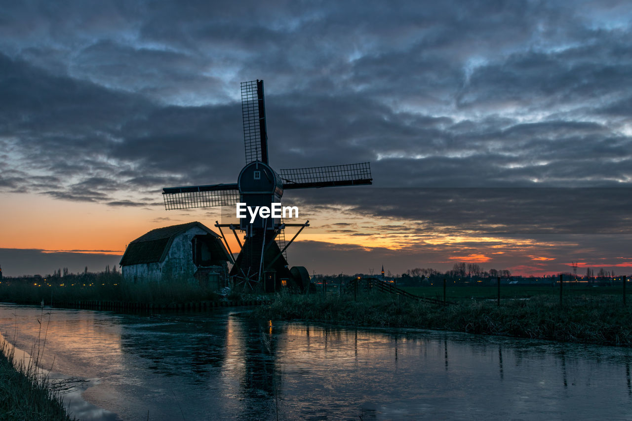 Dutch windmill and old house along a canal after sunset in winter