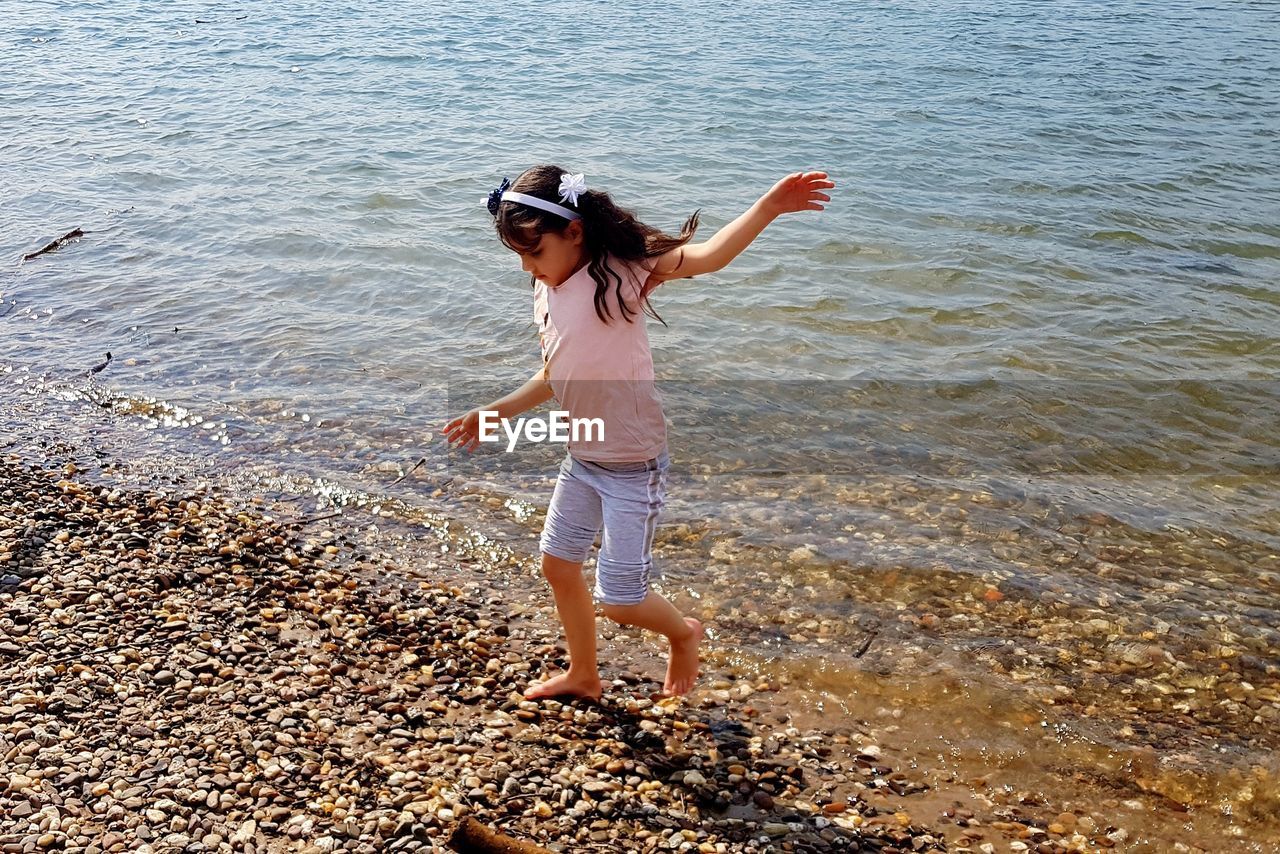 Full length of girl with arms outstretched walking at shore