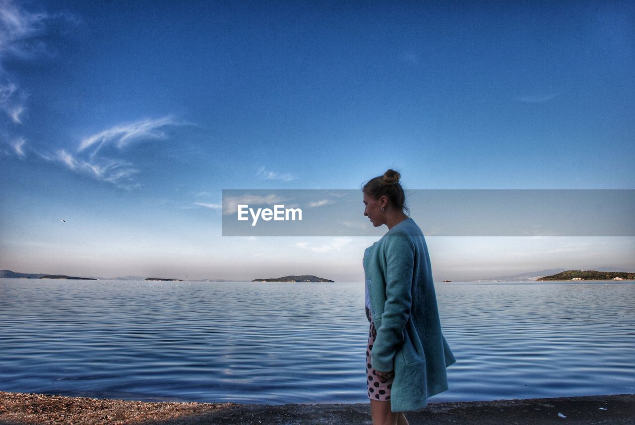 Side view of woman looking at sea against blue sky