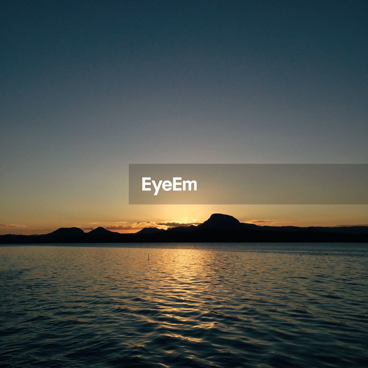 Scenic view of river and silhouette mountains against clear sky during sunset