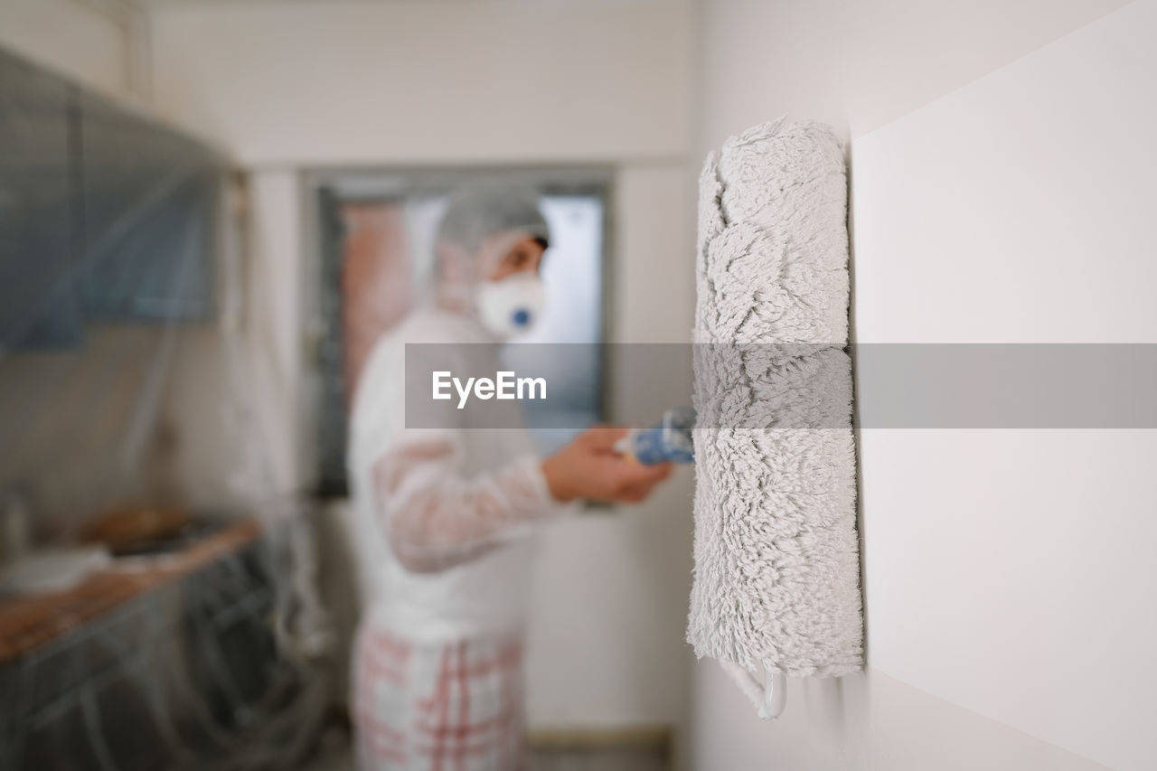 Side view of man working with paint roller and standing in kitchen