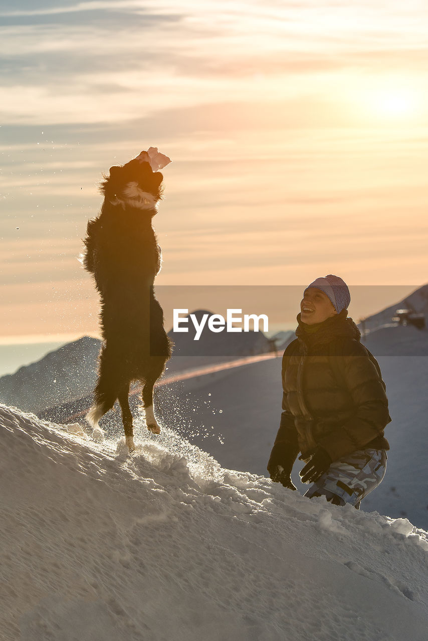 PEOPLE ON SNOW COVERED LAND AGAINST SKY AT SUNSET