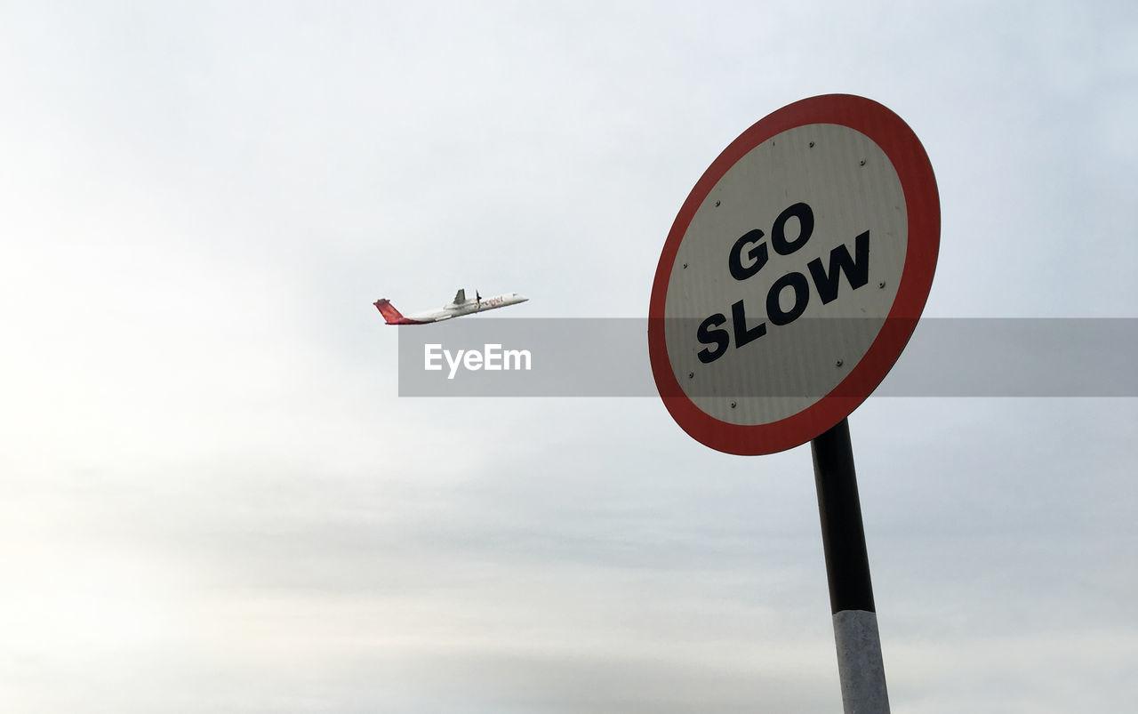 Low angle view of roadsign against airplane