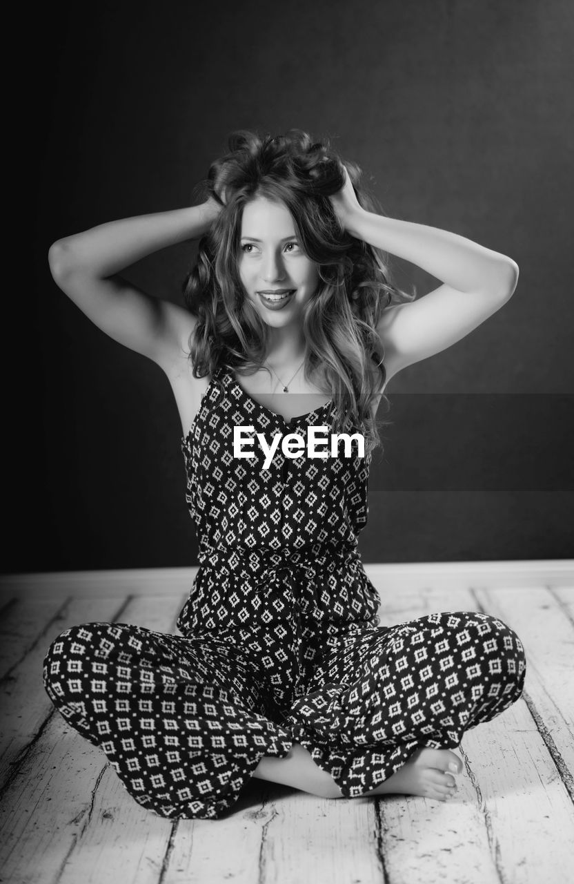 Young woman with hands in hair sitting on wooden floor