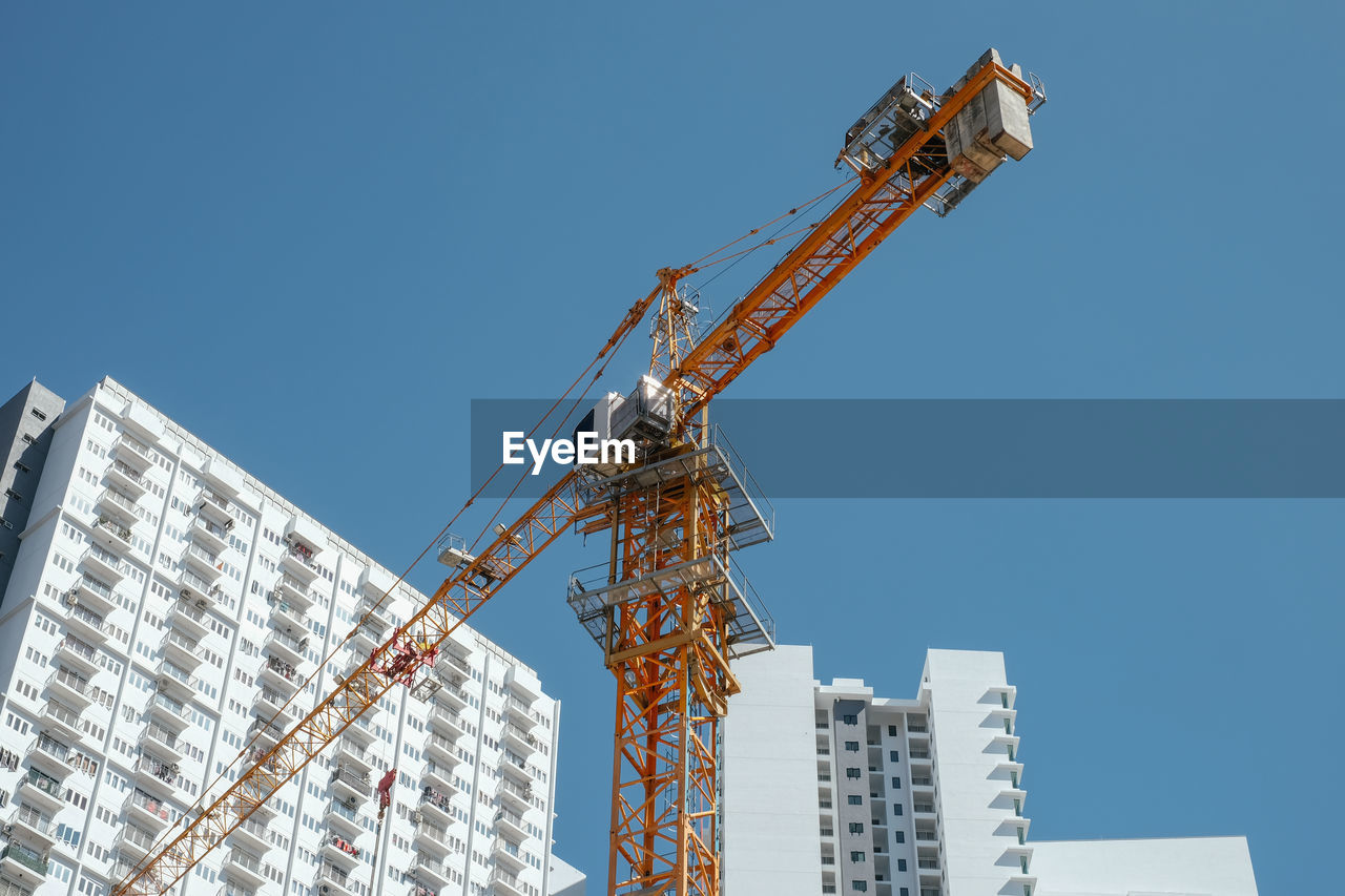 Low angle view of tower crane by building against clear sky