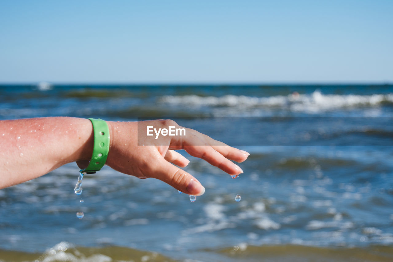 Cropped image of wet hand against sea