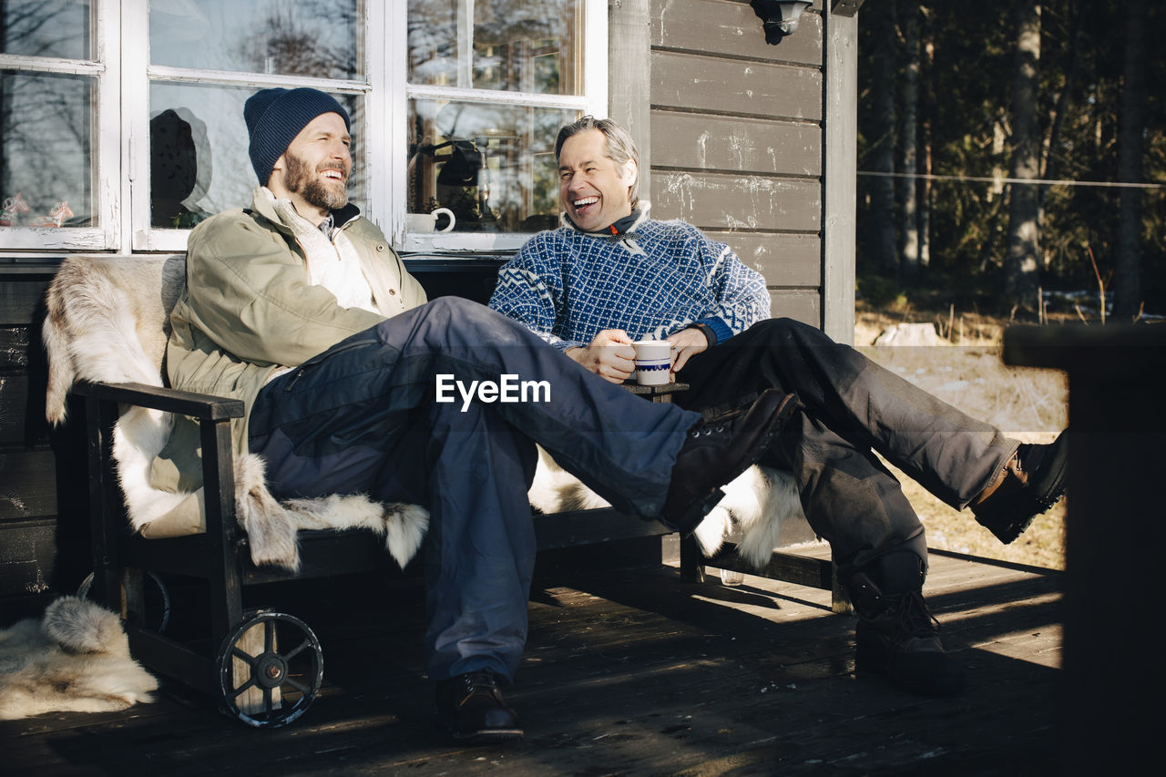 Cheerful mature men talking while having coffee together at porch during winter