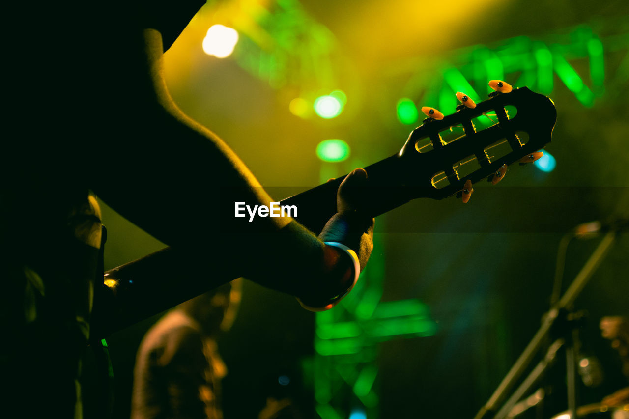Close up of a hand holding a guitar neck at a concert with green lights in the background