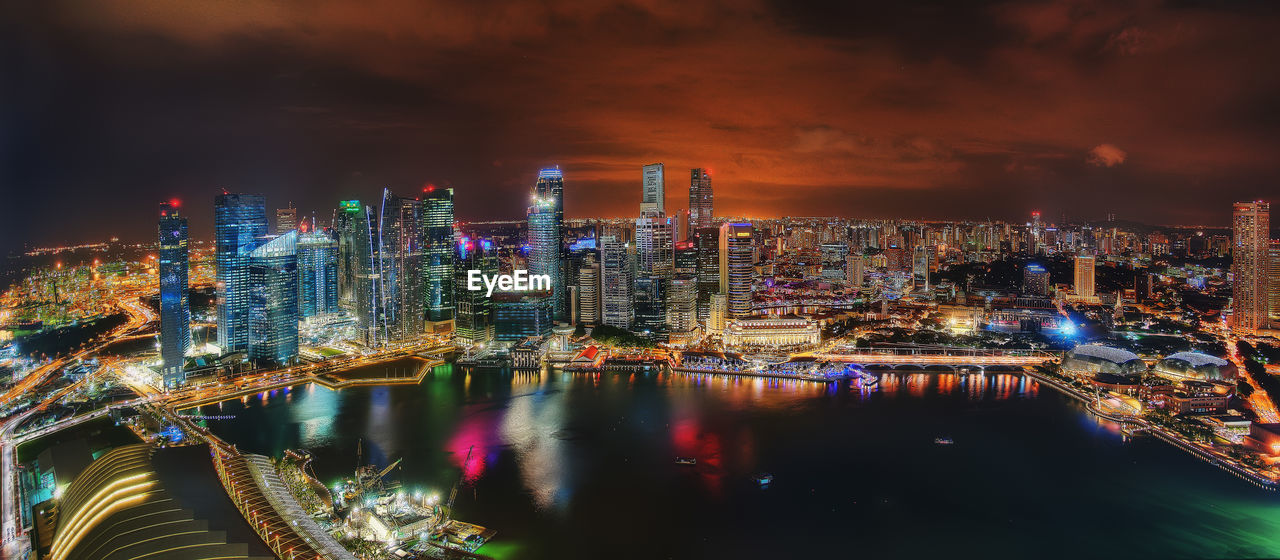 Illuminated city by river against sky at night