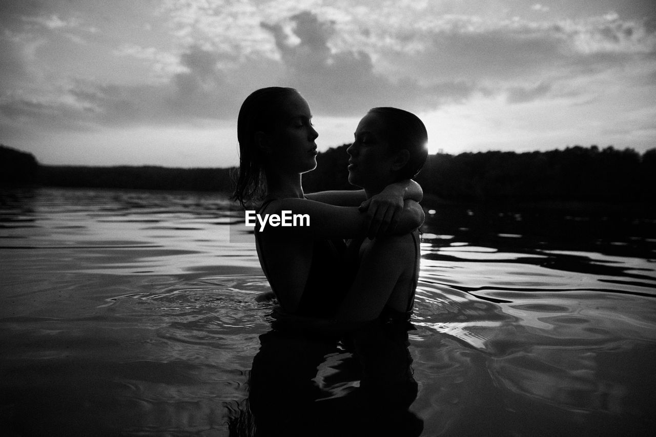 REAR VIEW OF MOTHER AND SON AT SWIMMING POOL AGAINST SKY