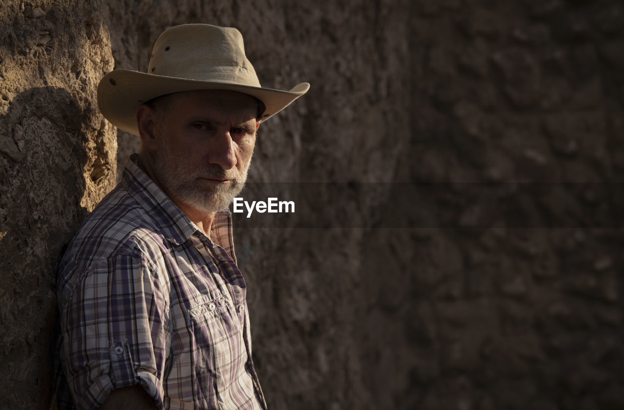 Portrait of adult man in cowboy hat and shirt against abandoned building