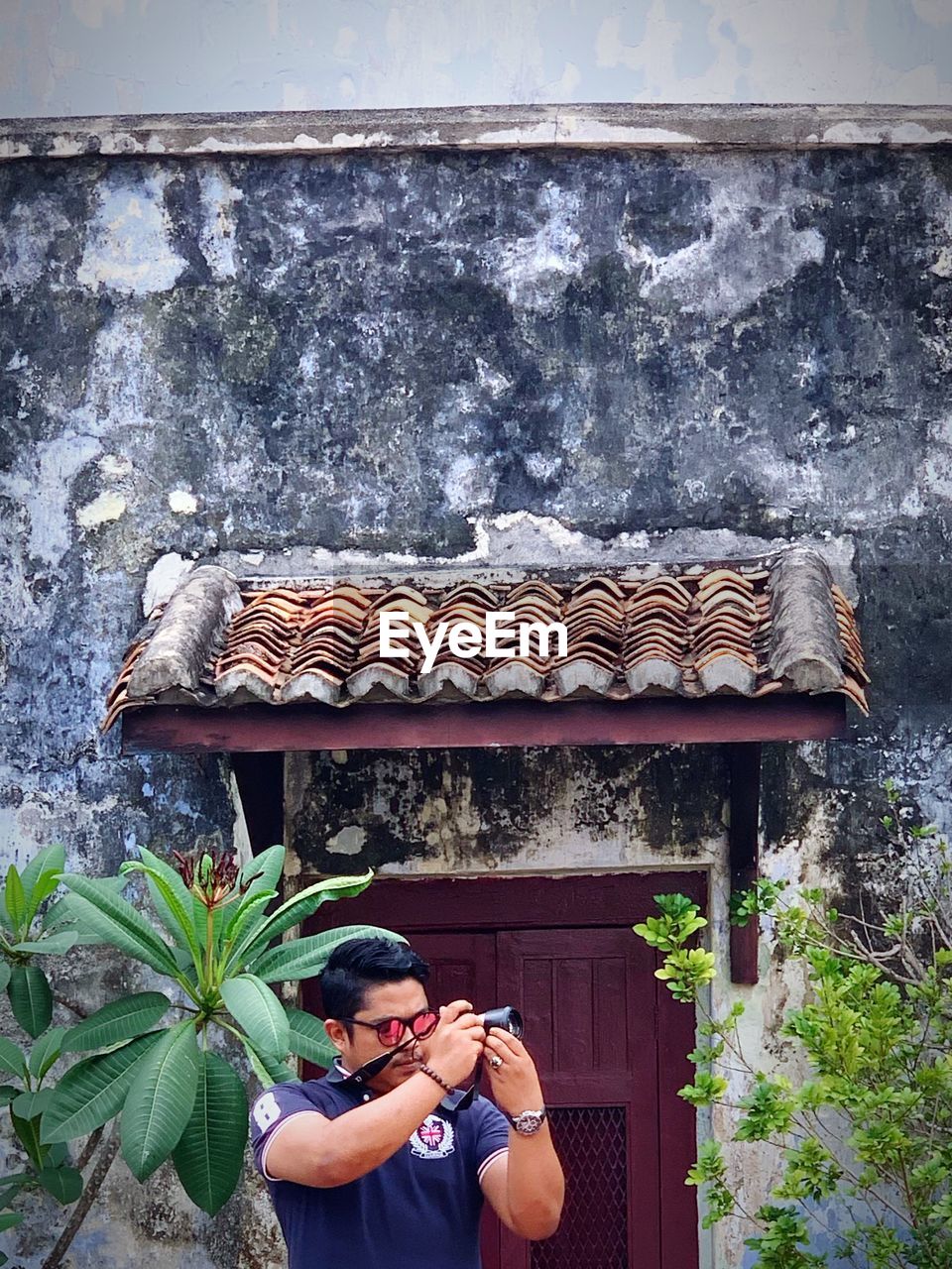 Young man photographing with camera while standing against house 