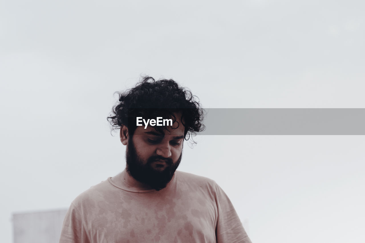 Thoughtful young bearded man standing against clear sky