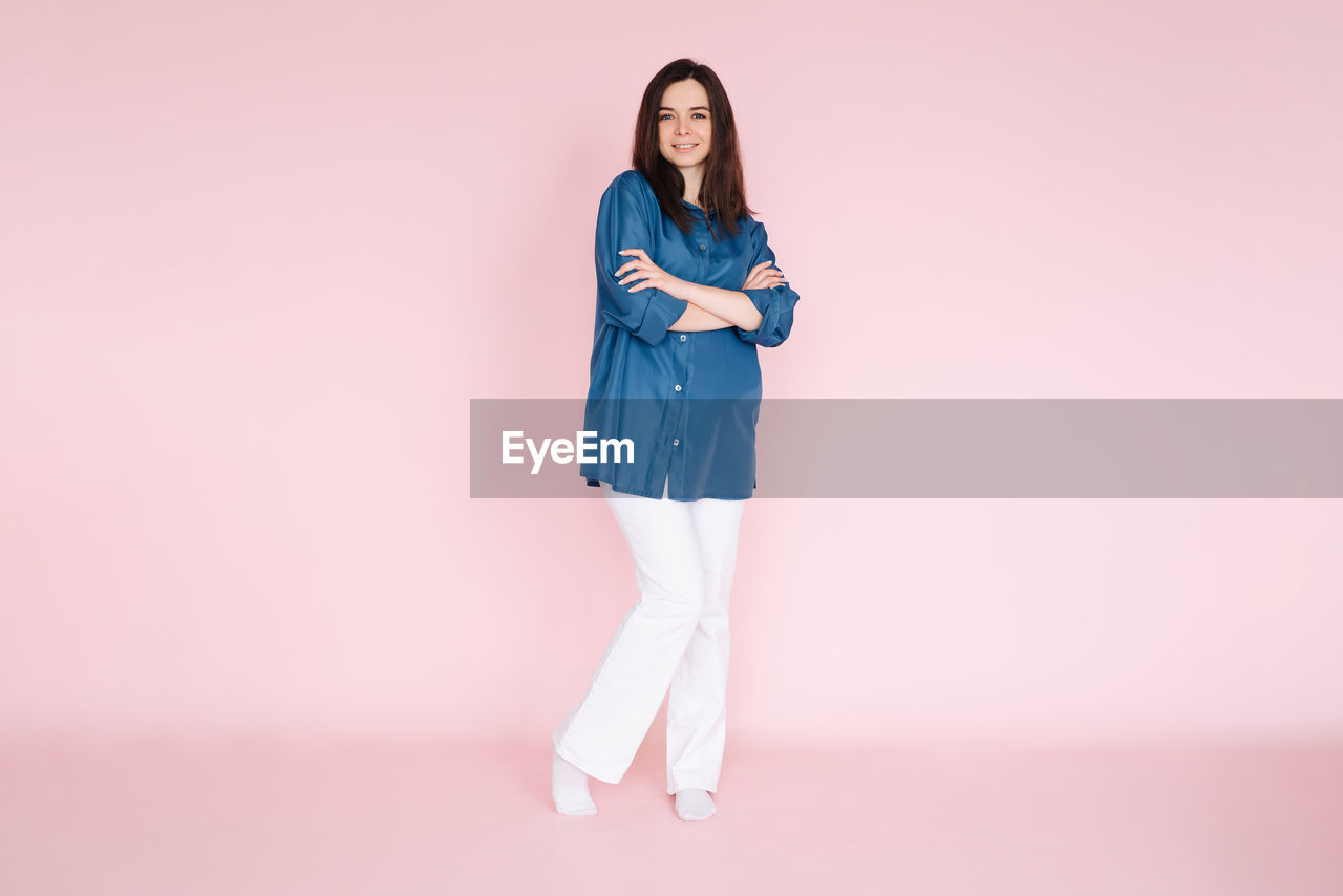 Confident businesswoman in stylish smart casual outfit, standing with folded hands, isolated on pink