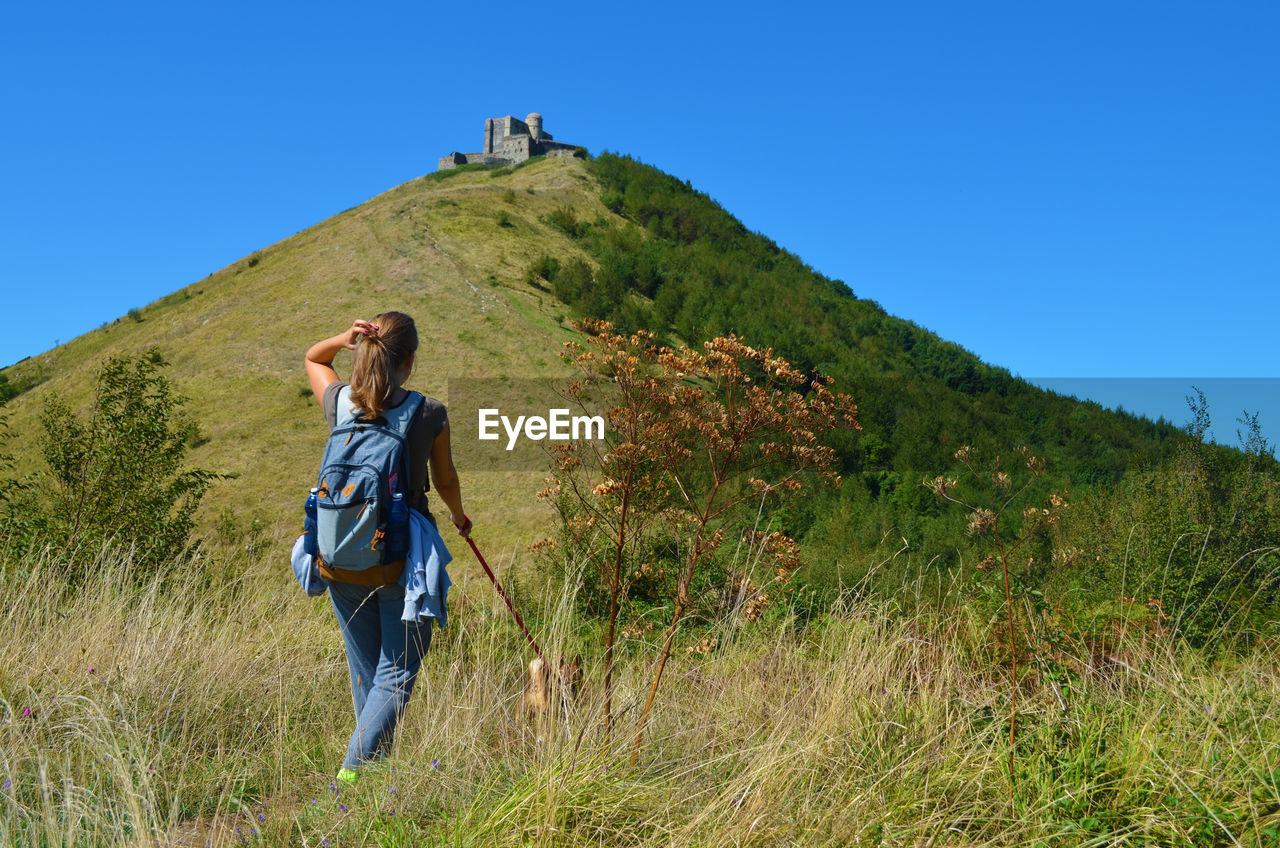 Rear view of woman hiking on grassy mountain against sky
