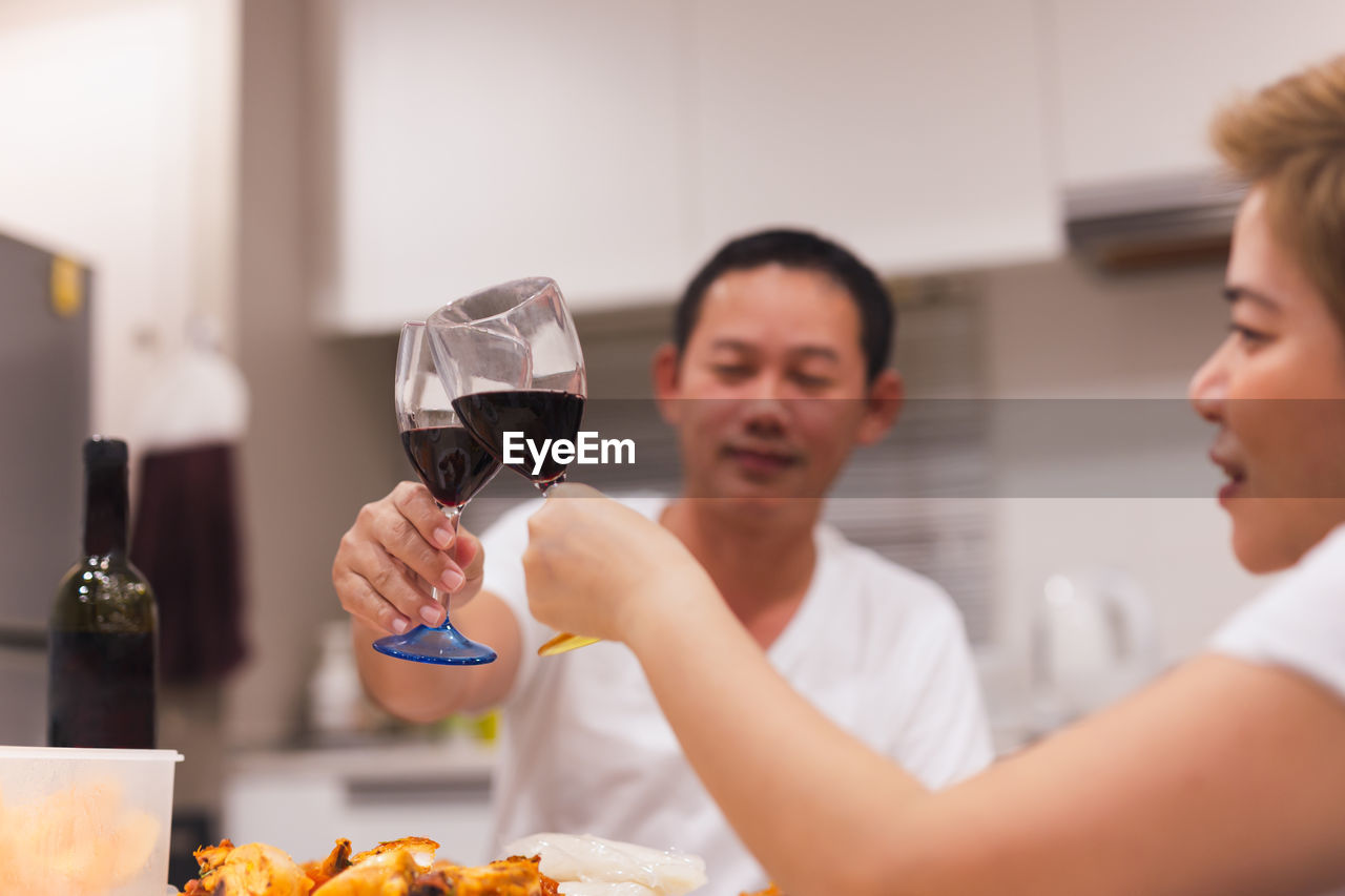 Sweet couple having dinner with toasting glasses of red wine at home.