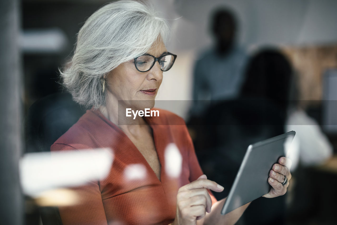 Senior businesswoman using tablet pc seen through glass window