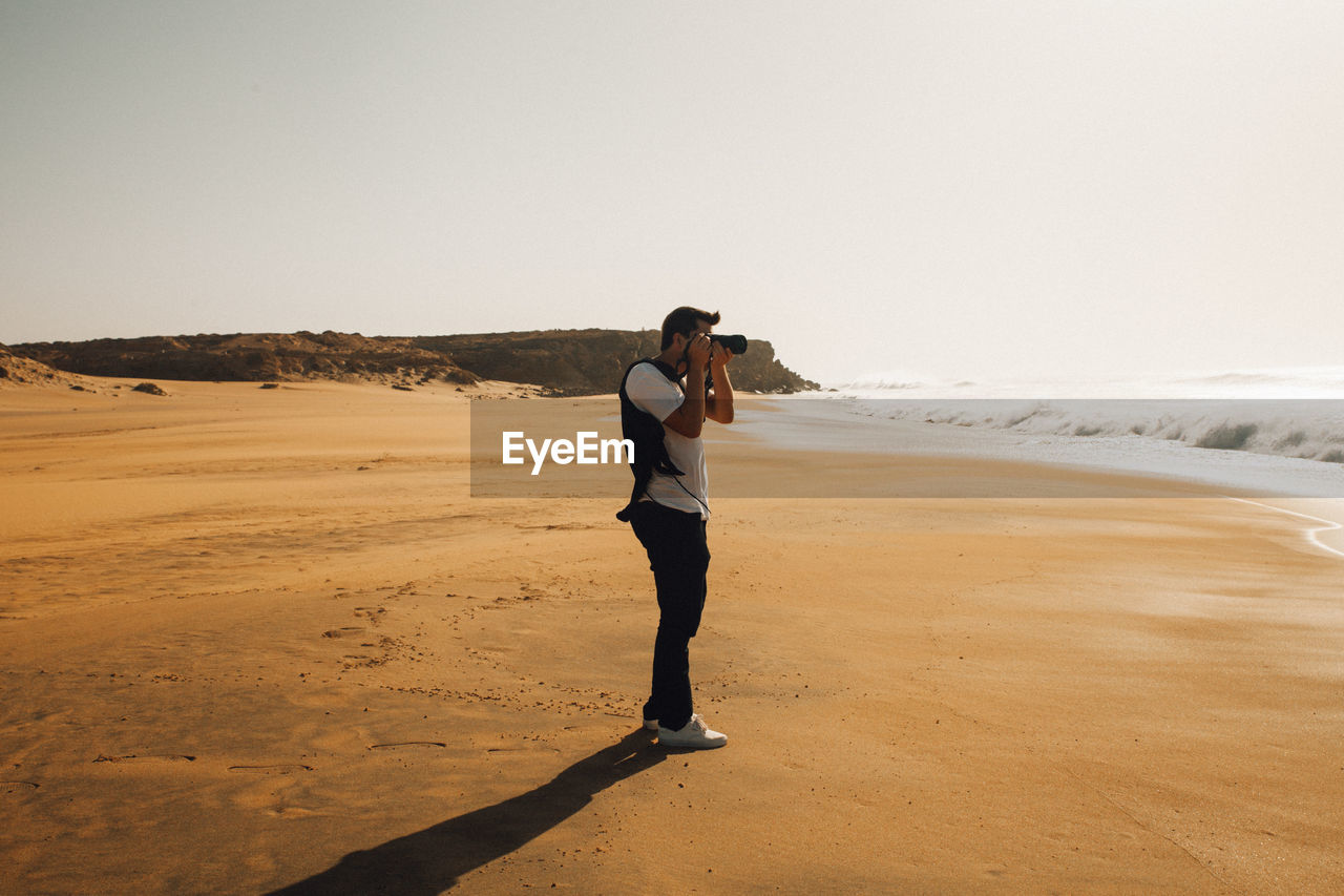 Man photographing at beach against sky