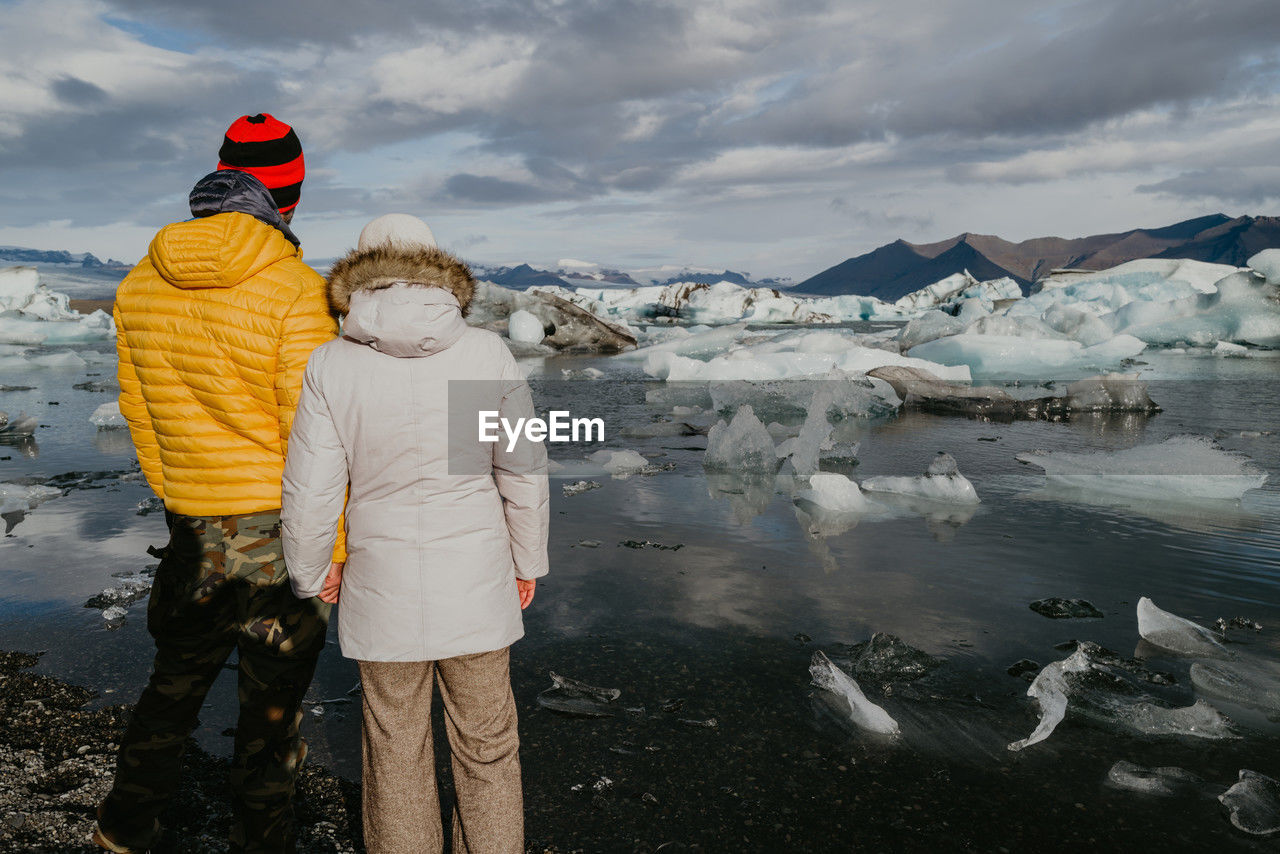 Couple in winter clothes standing overlooking jökulsárlón glacier lagoon in iceland