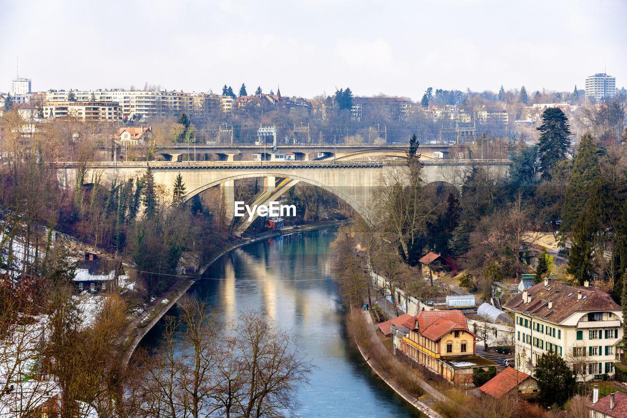 BRIDGE OVER RIVER AMIDST BUILDINGS IN CITY