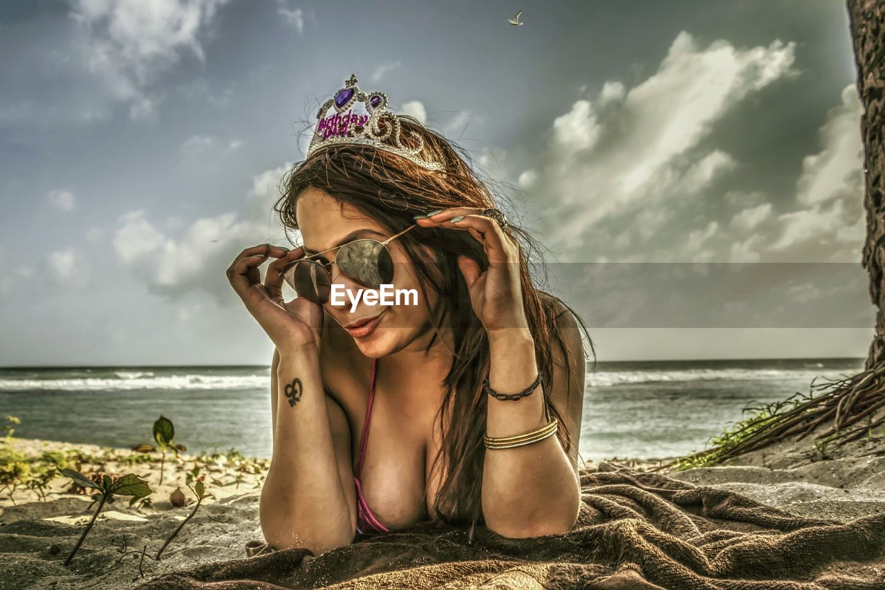 PORTRAIT OF YOUNG WOMAN WEARING SUNGLASSES ON BEACH