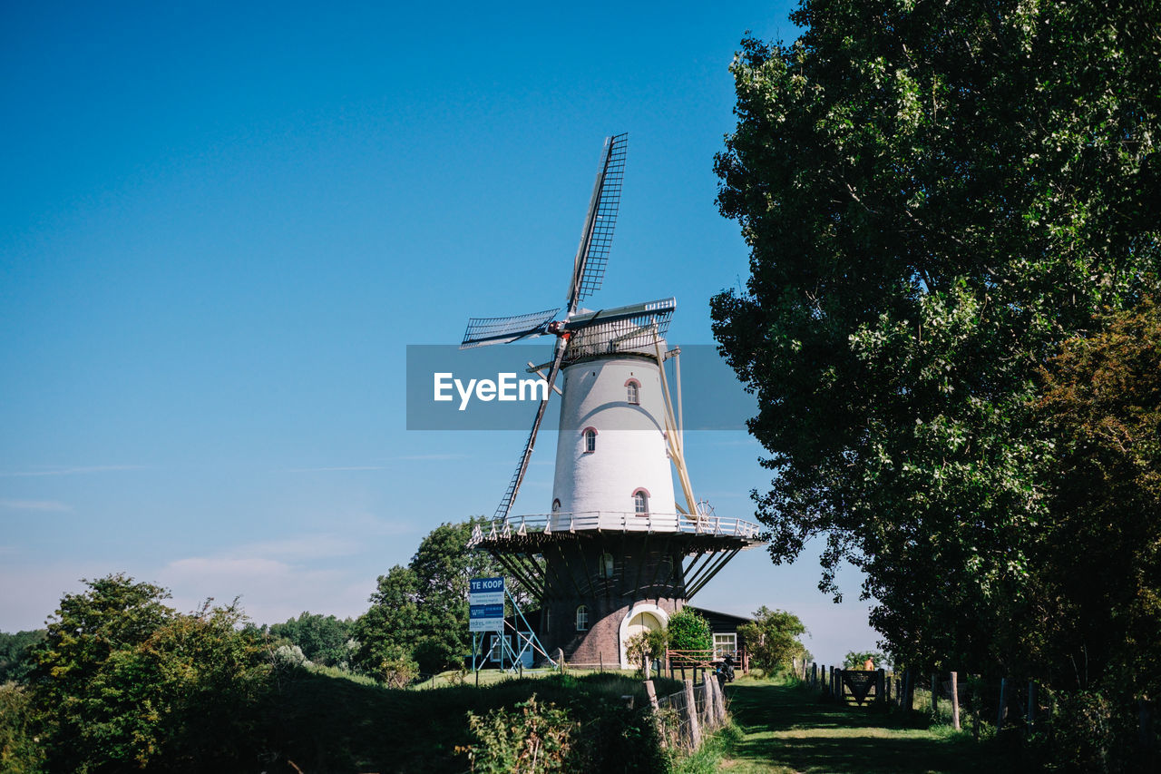 LOW ANGLE VIEW OF TRADITIONAL WINDMILL BY TREES AGAINST SKY