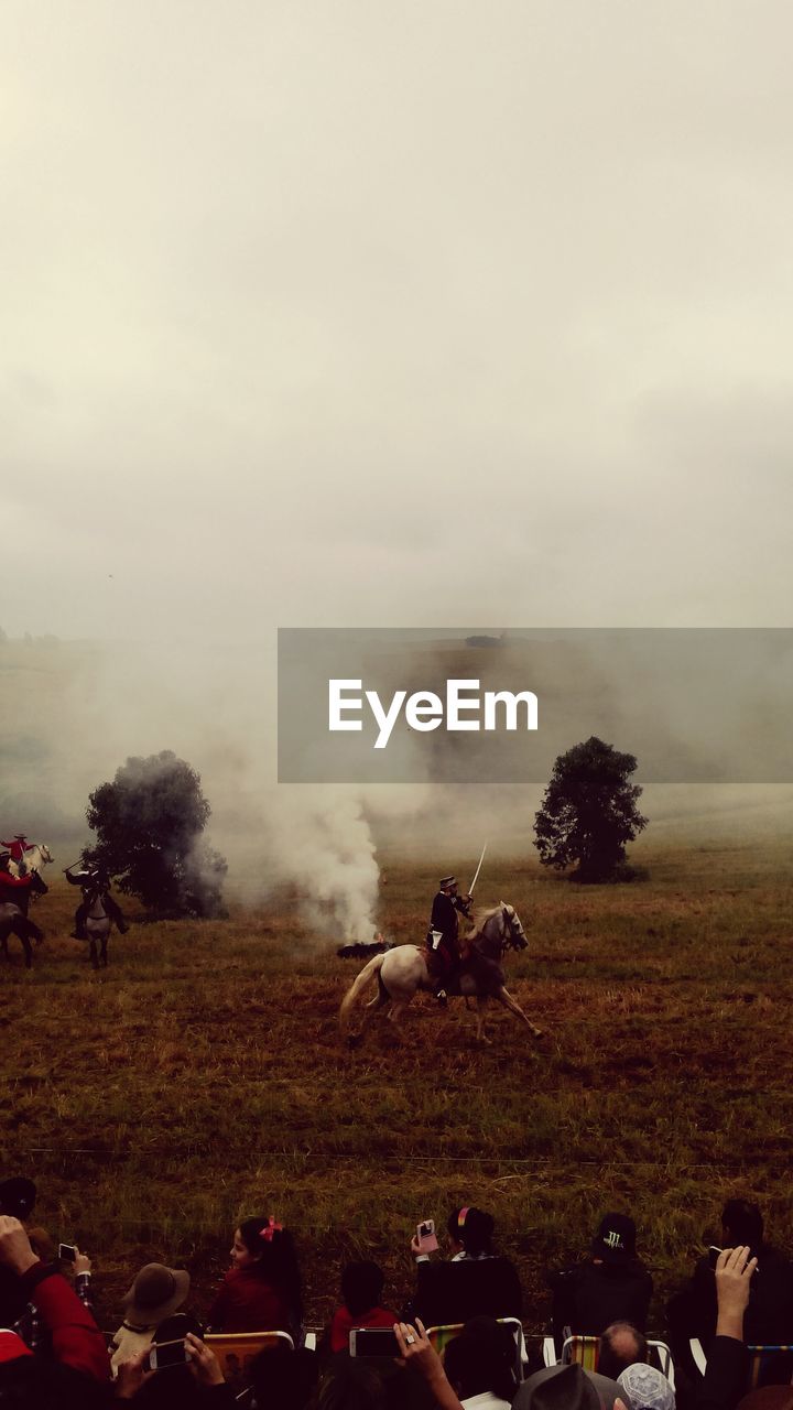 People riding horse on field against sky