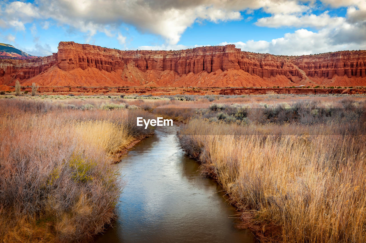 Water amidst grass against rock formation and sky