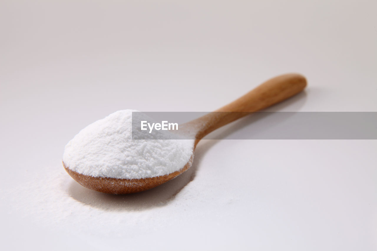 Close-up of baking soda in wooden spoon against white background