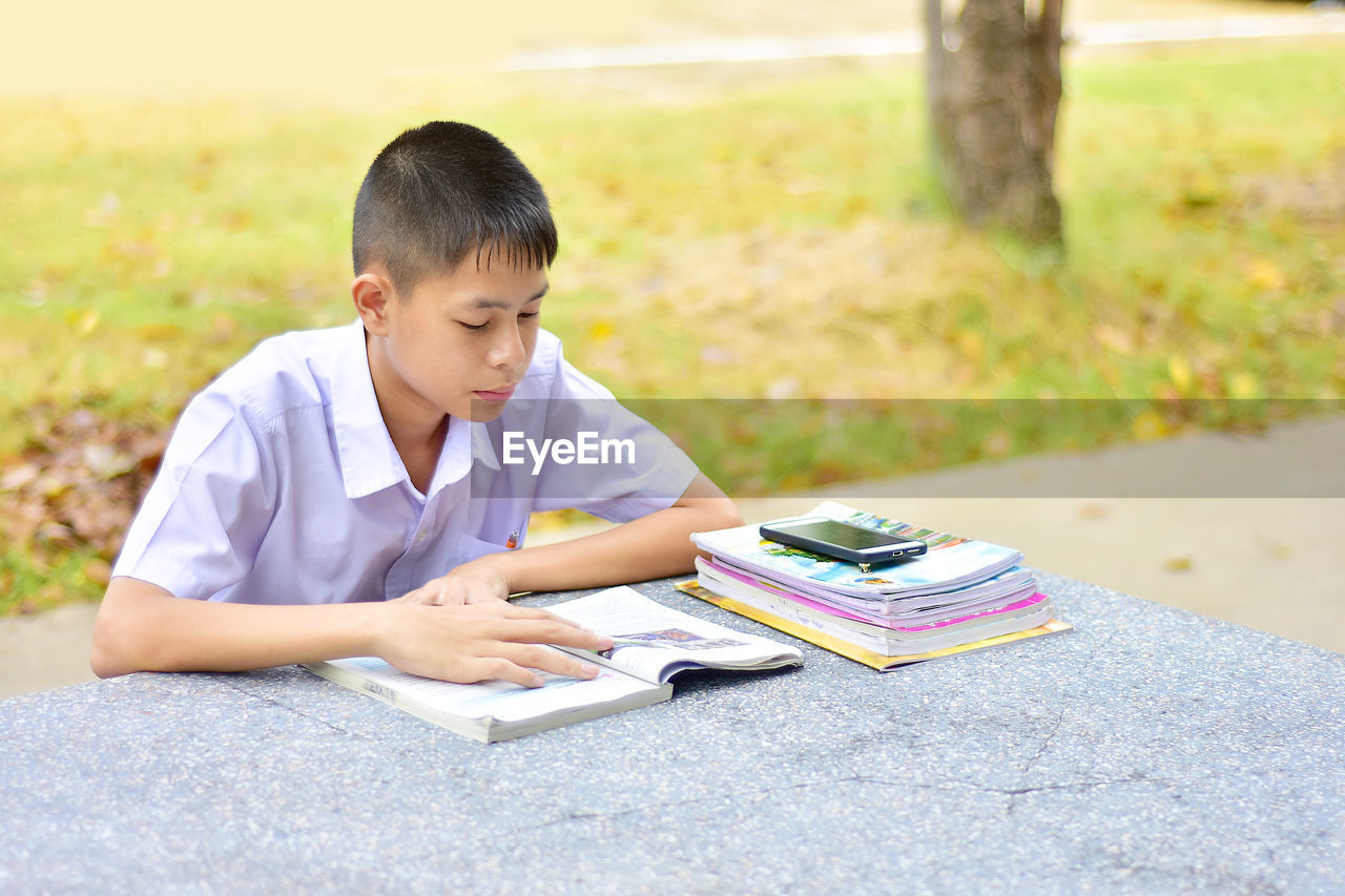 Boy reading book while sitting at park