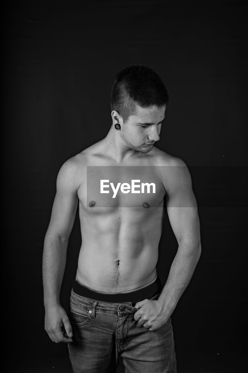 Shirtless man standing against black background