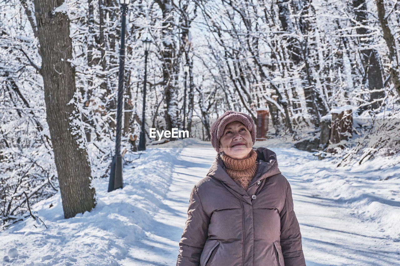  a  senior woman walking and looking up at something against the background of a winter snowy park