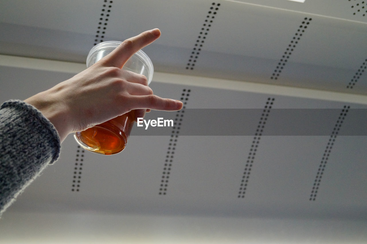 Cropped hand of woman holding drink against ceiling