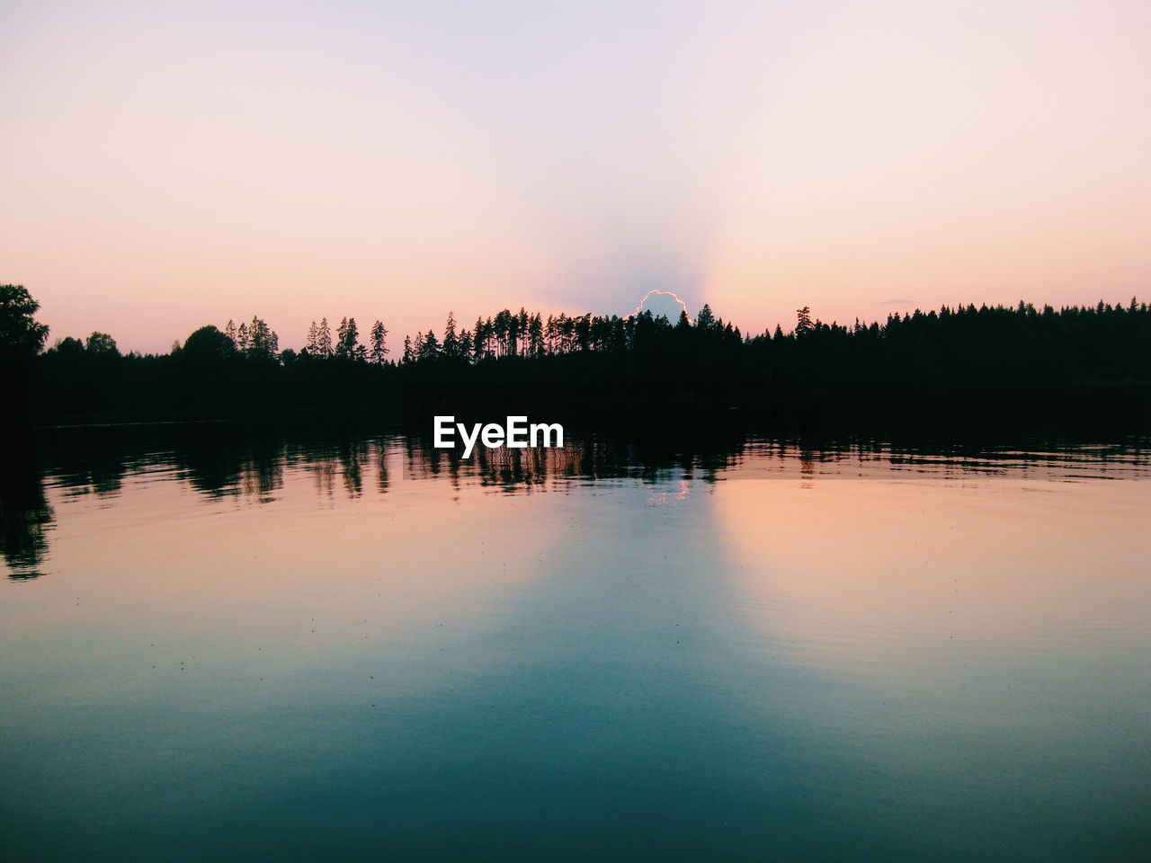 Silhouette trees by calm lake at sunset