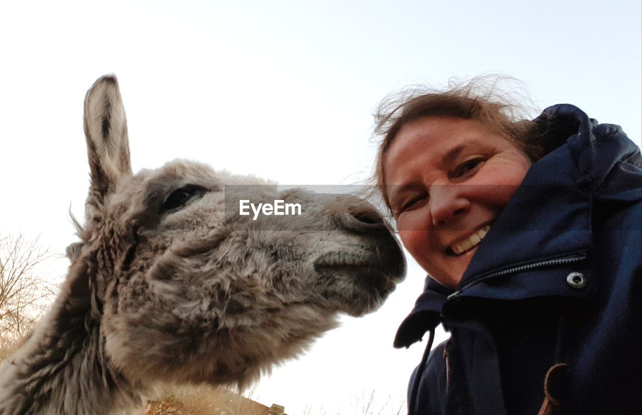 Portrait of smiling woman against clear sky with donkey