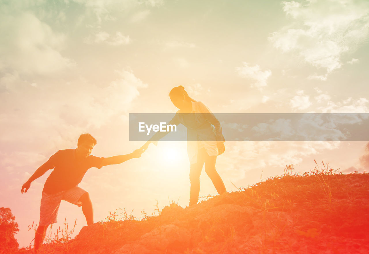 Silhouette couple holding hands on land against sky during sunset