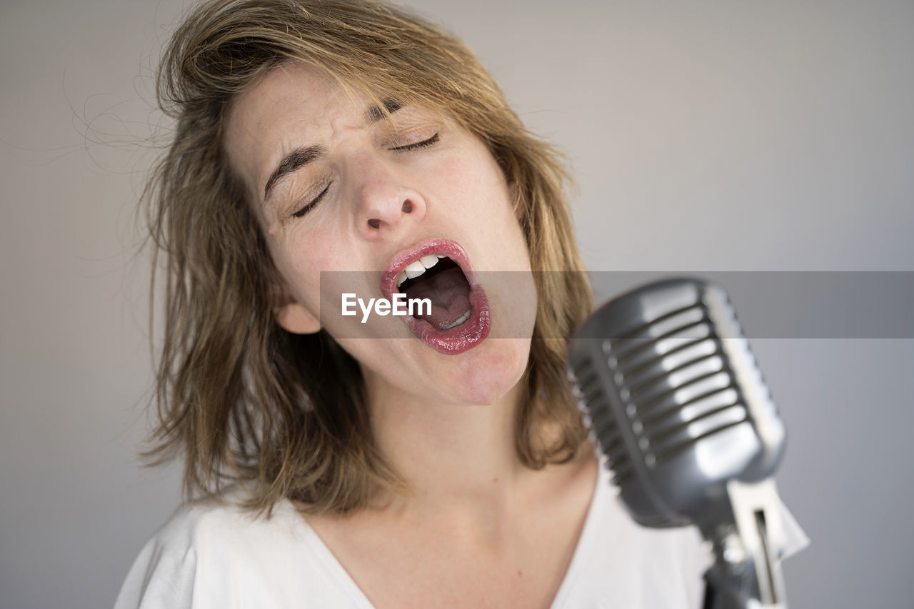 Close-up of woman singing against colored background