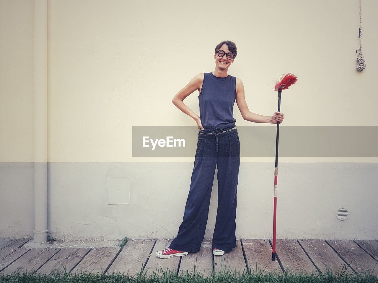 Portrait of smiling woman holding broom while standing against wall