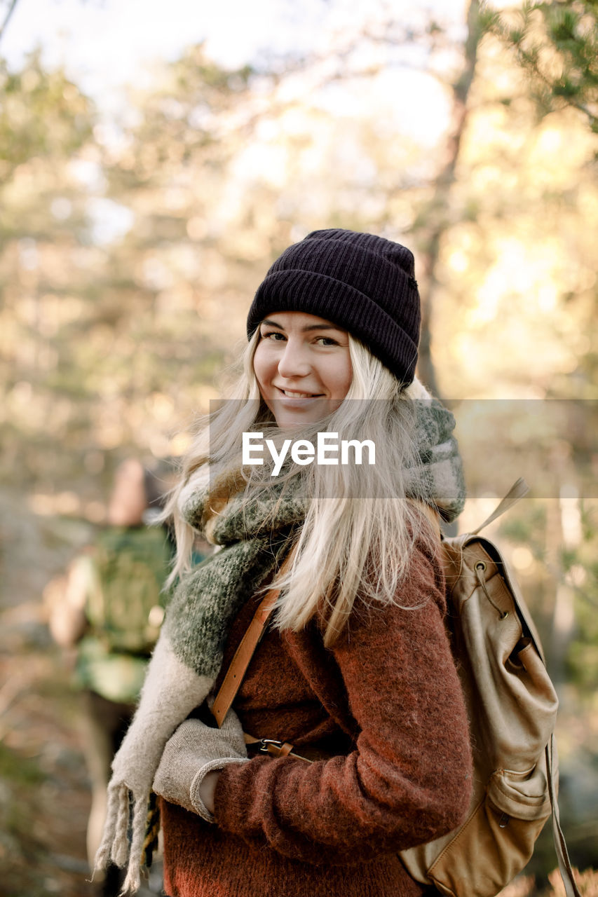 Side view of smiling young woman with backpack in forest