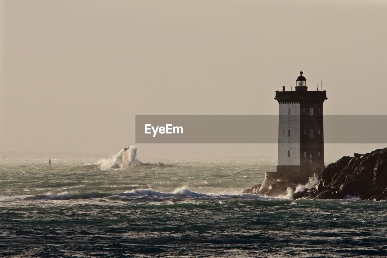 Lighthouse at sea shore against clear sky