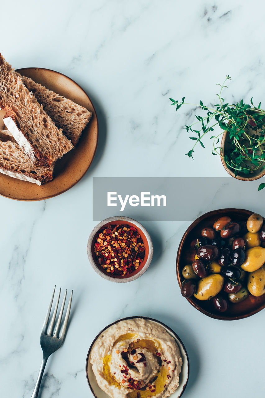 Hummus, mixed olives, and sourdough bread on a marble background