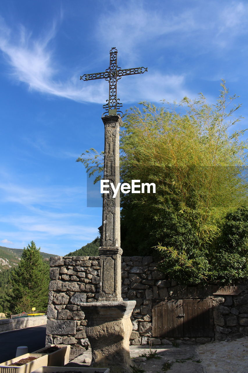 religion, sky, belief, spirituality, architecture, tree, built structure, nature, day, cross, cloud - sky, art and craft, no people, plant, place of worship, sunlight, sculpture, outdoors